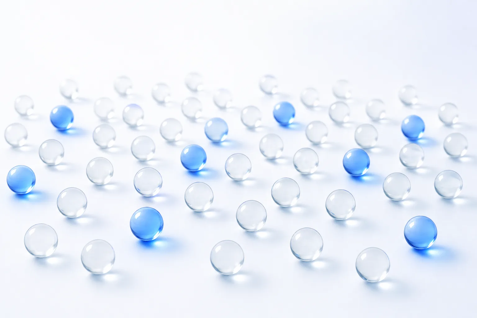 A wide field of small colourless glass spheres on white, with a distinct minority of them lit from within in electric blue and casting bright pools of light.